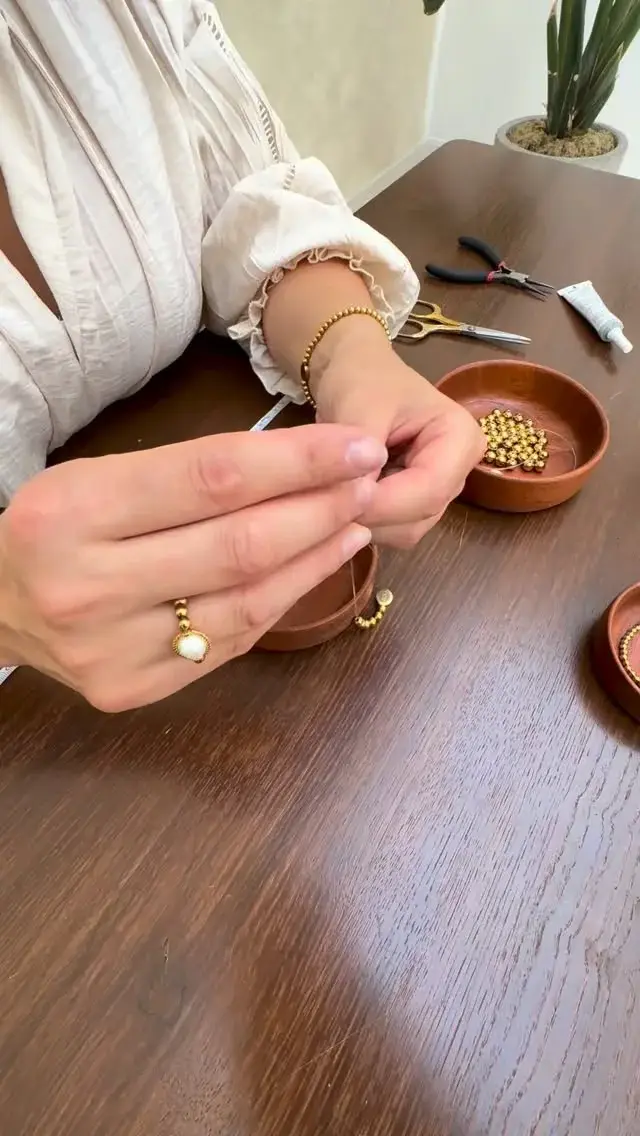 Close-up van handen die natuursteen kralen rijgen in het atelier